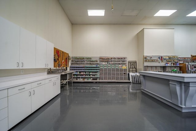 kitchen with a paneled ceiling, white cabinets, and concrete floors