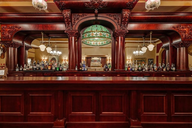 bar featuring an inviting chandelier, hanging light fixtures, and decorative columns