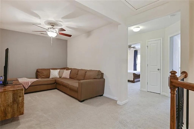 living area with baseboards, light colored carpet, attic access, and a ceiling fan