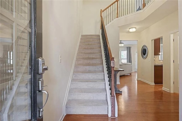 stairway with baseboards, a ceiling fan, wood finished floors, and a towering ceiling