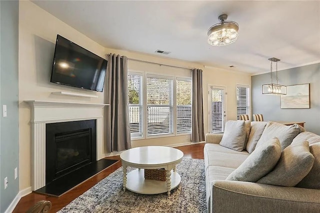 living room featuring dark wood-style floors, visible vents, a fireplace with raised hearth, and baseboards