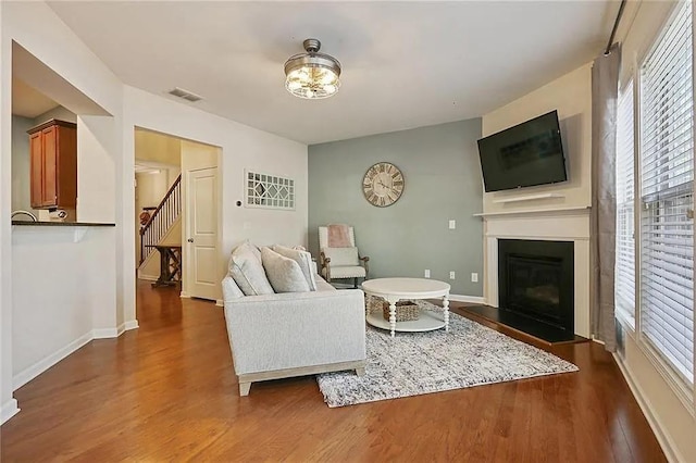 living room with dark wood-style floors, visible vents, baseboards, a fireplace with flush hearth, and stairs