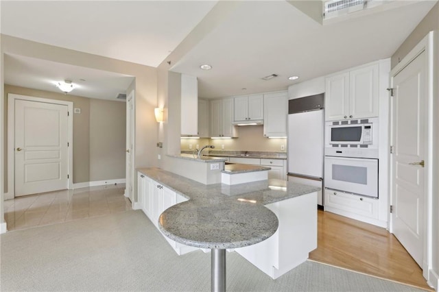 kitchen with built in appliances, a peninsula, white cabinetry, light stone countertops, and recessed lighting