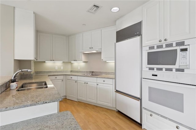 kitchen featuring built in appliances, a sink, white cabinetry, light wood-style flooring, and light stone countertops