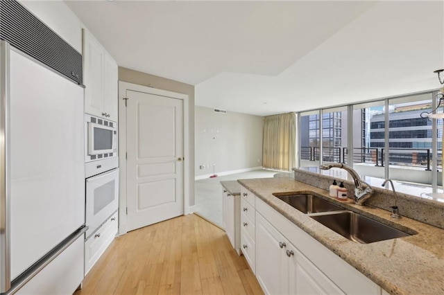 kitchen with built in appliances, a sink, light wood finished floors, and white cabinetry