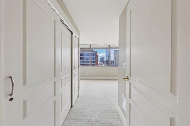 corridor featuring light colored carpet, baseboards, and a view of city
