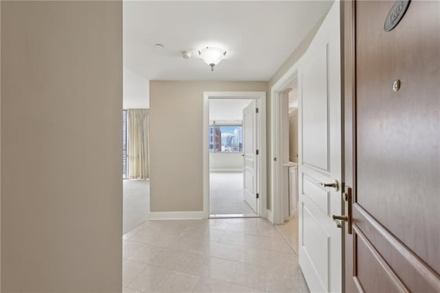 hall featuring baseboards, light tile patterned floors, and light colored carpet