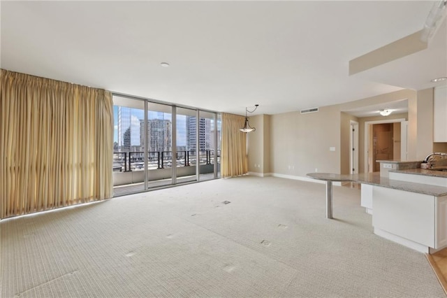 unfurnished living room with light carpet, a sink, and baseboards