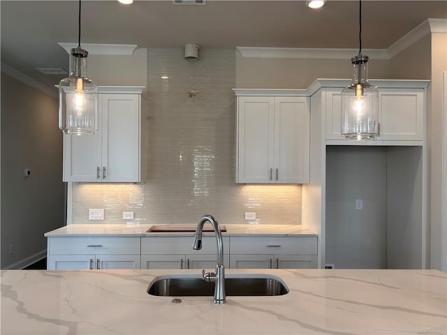 kitchen with a sink, crown molding, backsplash, light stone countertops, and white cabinets