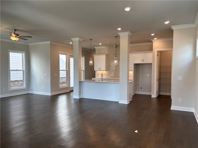 unfurnished living room featuring ceiling fan, healthy amount of natural light, a sink, crown molding, and baseboards