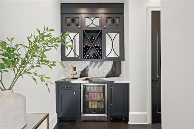 bar featuring beverage cooler, wet bar, a sink, decorative backsplash, and dark wood-type flooring