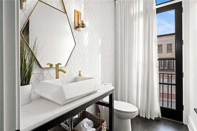 bathroom featuring a sink, toilet, wood finished floors, and wallpapered walls