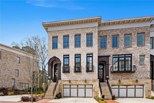 view of property featuring brick siding, stairway, driveway, and a garage