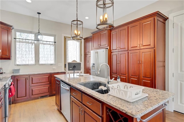 kitchen featuring stainless steel appliances, a sink, light stone countertops, an island with sink, and pendant lighting