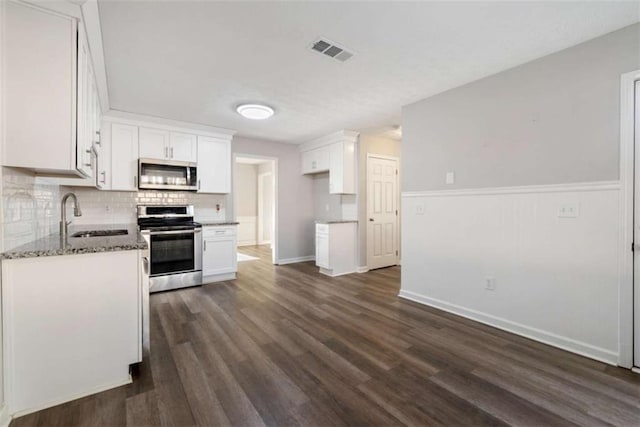 kitchen with white cabinetry, stainless steel appliances, sink, and dark stone countertops