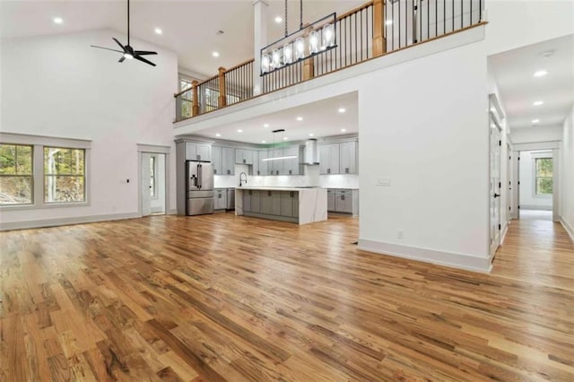 unfurnished living room featuring light wood finished floors, baseboards, ceiling fan, a high ceiling, and a sink