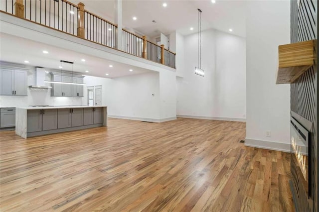 unfurnished living room featuring light wood finished floors, recessed lighting, a towering ceiling, and baseboards