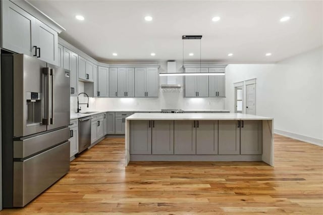 kitchen with stainless steel appliances, a sink, light wood-style floors, wall chimney range hood, and gray cabinets