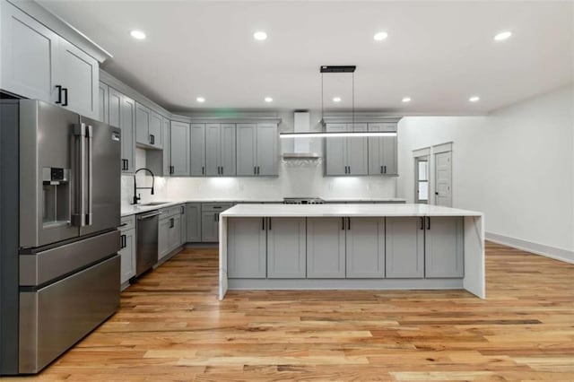 kitchen featuring light wood finished floors, a large island, gray cabinets, stainless steel appliances, and light countertops