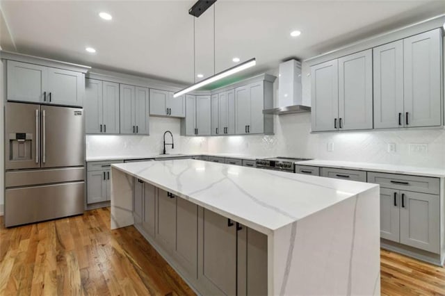 kitchen featuring wall chimney exhaust hood, a center island, gray cabinetry, stainless steel refrigerator with ice dispenser, and a sink