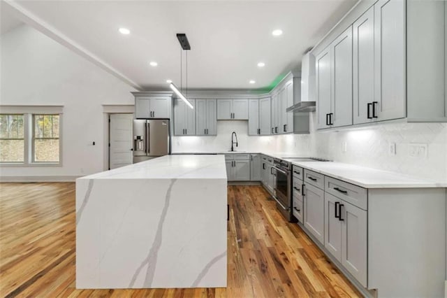 kitchen featuring lofted ceiling, gray cabinetry, appliances with stainless steel finishes, a center island, and wall chimney exhaust hood