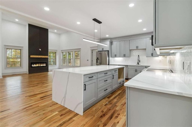 kitchen with a large fireplace, stainless steel refrigerator with ice dispenser, light wood-style floors, and gray cabinetry