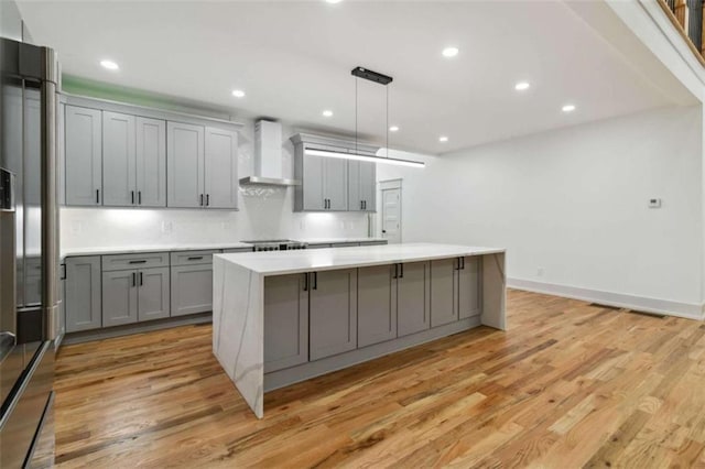 kitchen with light wood-style flooring, wall chimney exhaust hood, a center island, gray cabinets, and light countertops