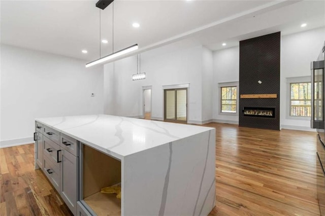 kitchen with a large fireplace, light wood-style flooring, decorative light fixtures, light stone countertops, and gray cabinetry