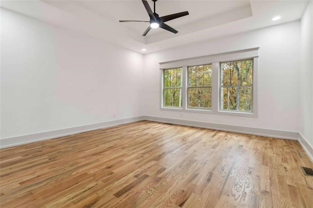 empty room with recessed lighting, wood finished floors, a ceiling fan, baseboards, and a raised ceiling