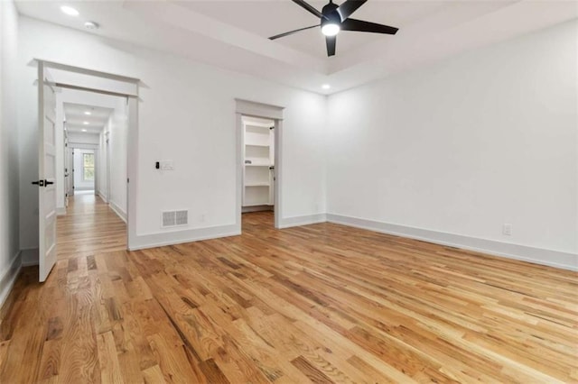 unfurnished bedroom with a walk in closet, a tray ceiling, visible vents, light wood-type flooring, and baseboards