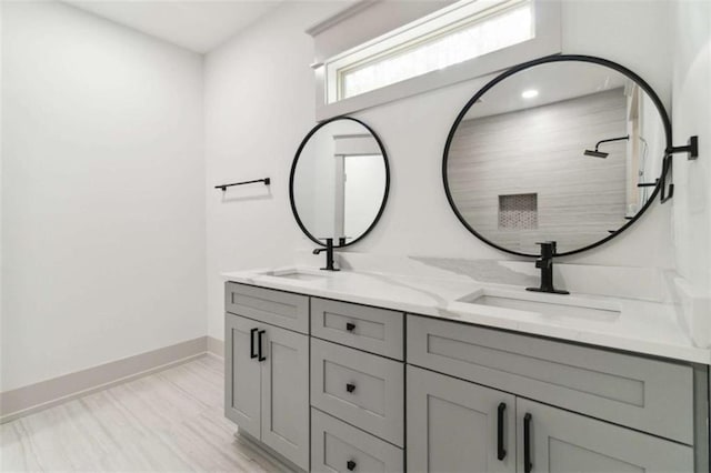 full bathroom with double vanity, baseboards, a tile shower, and a sink