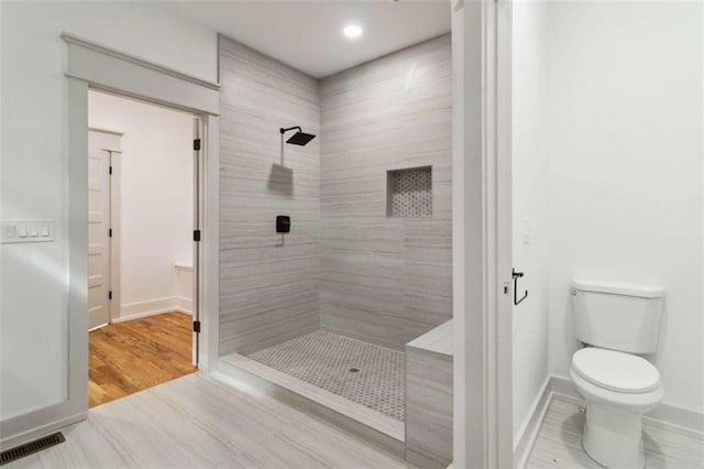 full bath featuring visible vents, tiled shower, toilet, and baseboards