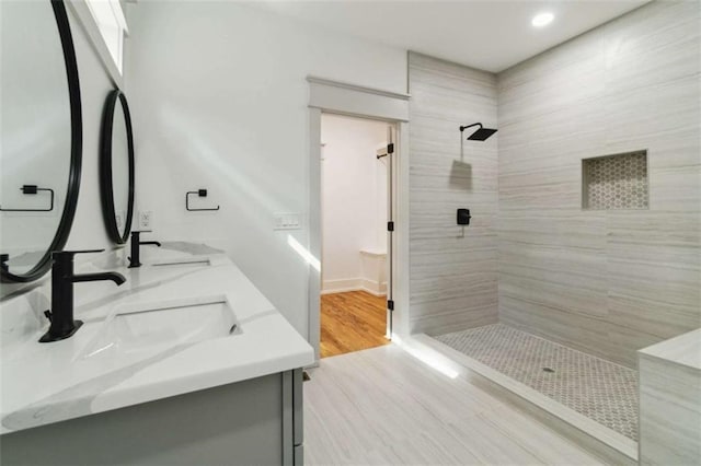 bathroom featuring double vanity, recessed lighting, a tile shower, a sink, and wood finished floors