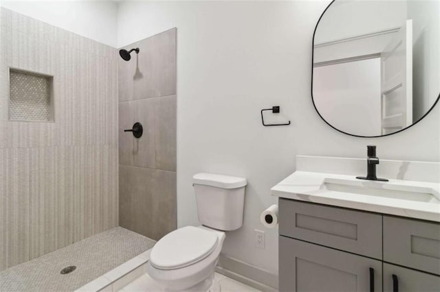 bathroom with toilet, baseboards, a tile shower, and vanity