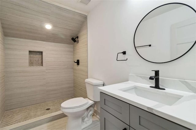 bathroom with toilet, vaulted ceiling, tiled shower, and vanity