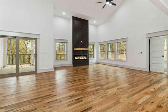 unfurnished living room with a large fireplace, high vaulted ceiling, wood finished floors, and baseboards