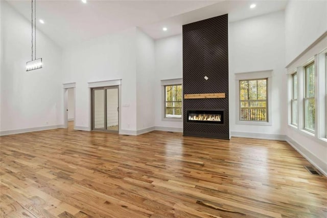 unfurnished living room featuring a large fireplace, visible vents, a towering ceiling, and wood finished floors