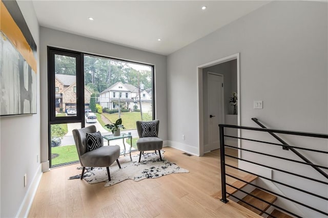 living area featuring visible vents, baseboards, recessed lighting, light wood-style floors, and an upstairs landing