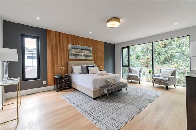 bedroom with light wood finished floors, wooden walls, an accent wall, baseboards, and recessed lighting