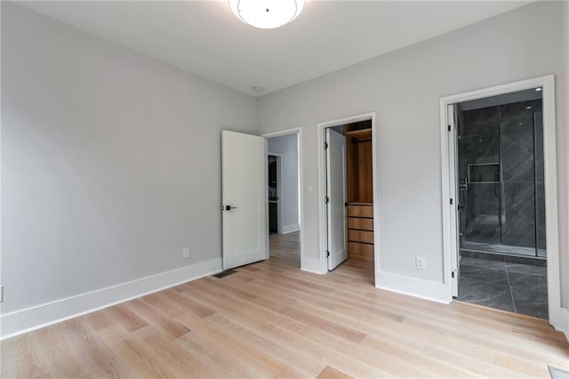 unfurnished bedroom with light wood-type flooring, baseboards, and ensuite bath