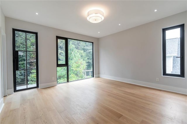 unfurnished room featuring recessed lighting, light wood-type flooring, plenty of natural light, and baseboards