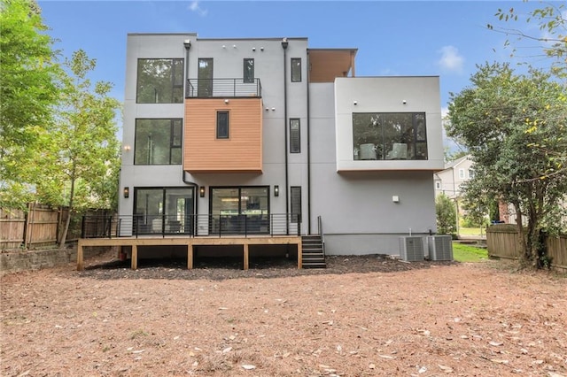 back of property with stucco siding, a balcony, central AC unit, and fence