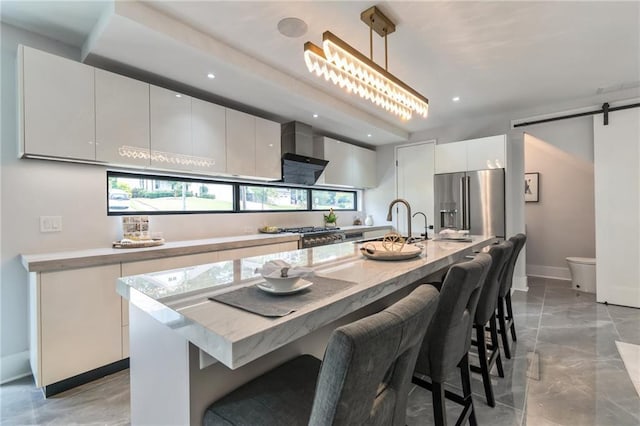 kitchen featuring stainless steel appliances, hanging light fixtures, white cabinets, a kitchen bar, and a barn door