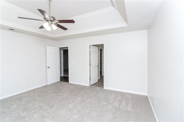 unfurnished bedroom with a raised ceiling, ceiling fan, and light carpet