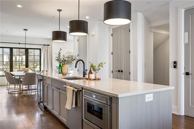 726 Edgewood Ave NE, Atlanta, GA 30307 - kitchen with an island with sink, stainless steel dishwasher, dark wood-style flooring, a sink, and gray cabinetry