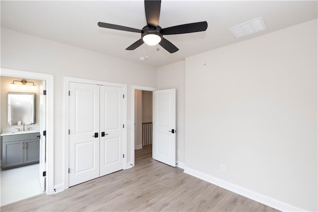 unfurnished bedroom with connected bathroom, sink, ceiling fan, light wood-type flooring, and a closet