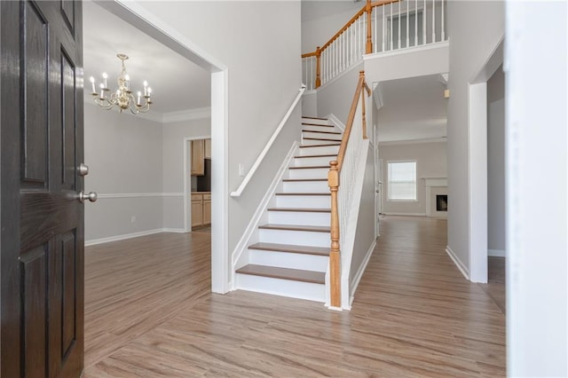 foyer entrance with a fireplace, crown molding, light wood-style flooring, baseboards, and stairs