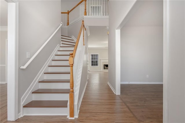 staircase featuring a fireplace, wood finished floors, a towering ceiling, and baseboards