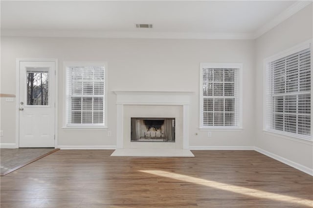 unfurnished living room with visible vents, crown molding, a fireplace with raised hearth, and wood finished floors