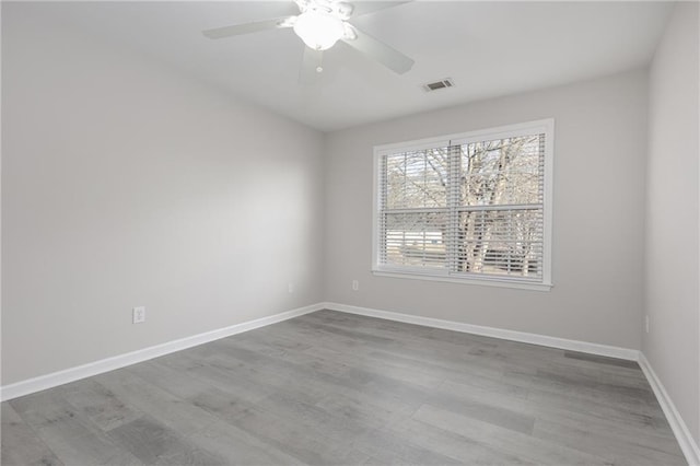 spare room with a ceiling fan, wood finished floors, visible vents, and baseboards